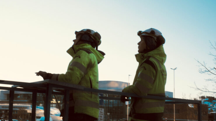Two people in fluorescent high-visibility jackets at dusk, illustrating day-and-night EN 17353 Type AB3 visibility