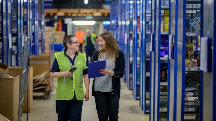 Warehouse staff in high-visibility vests walking through a storage aisle