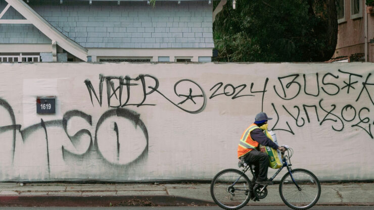 Cyclist in an orange high-visibility vest riding past a city wall