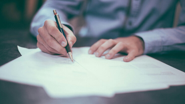 Hand signing a document with a pen on a desk