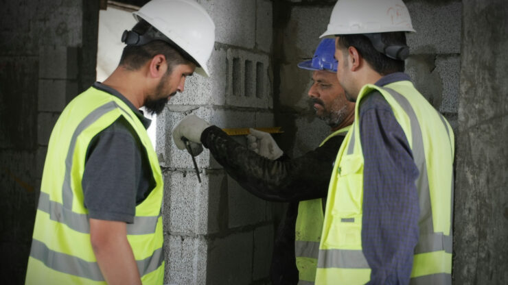 Construction workers in high-visibility vests with reflective stripes measuring on site